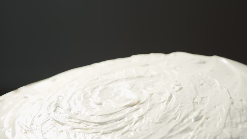 A hand puts two fused red cherries on a homemade white cake that rotates at an angle close up