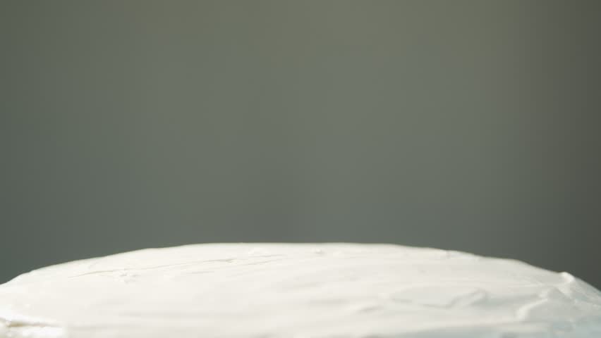 A hand puts two fused red cherries on a white cake close-up