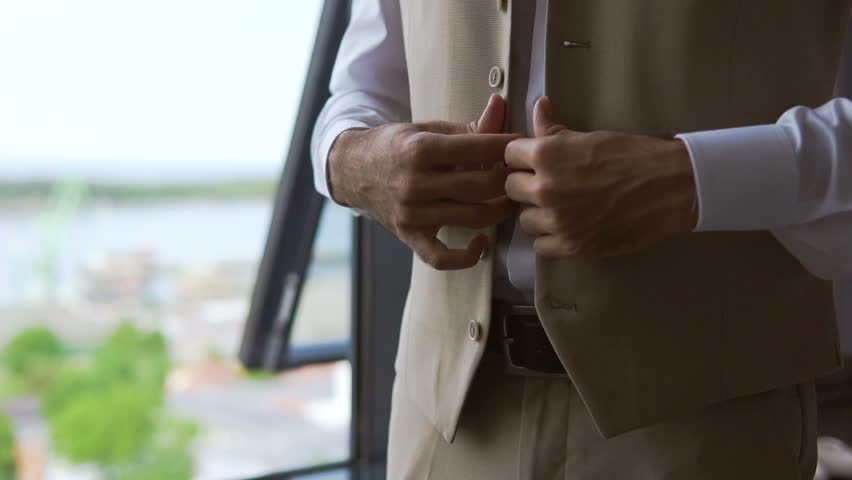 Hands adjust the belt. A young businessman puts on a suit before an important meeting. The manager gets dressed near the window in the morning before work. Fingers fasten buttons on a jacket or vest