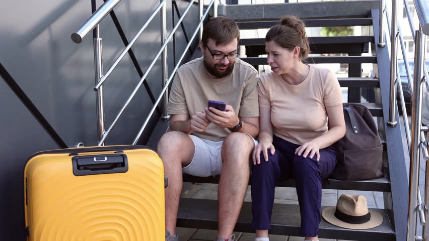 Happy couple sitting and buying plane tickets on the street. They rejoice at a successful purchase. They give each other high-fives. Concept: good news, purchase, ready to travel, obtaining a visa