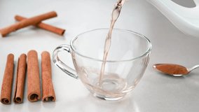Serving cinnamon water in a glass cup with cinnamons in the background.