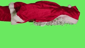 Vertical video Profile of father christmas with painful headache standing in studio over greenscreen backdrop, unwell man in saint nick red suit. Sick festive character with migraine feeling hurt