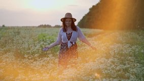Caucasian woman in a hat dancing in a field at sunset. Concept of smiles and happy free girl who feels freedom moving in a dance on the grass in nature. High quality 4k footage