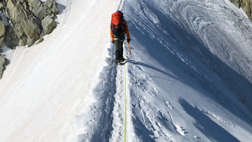 Сlimber walking narrow path on mountain ridge under Aiguille du Midi 3842m with French Alps mountains peaks panorama. Beauty of Nature and extreme people activity concept