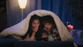 Couple Indian man and Arabian Hispanic woman night dating in bed under blanket family boyfriend girlfriend shocked watching horror film movie scared afraid frightened video with mobile phone hiding - Powered by Shutterstock - Get 15% off with code: PIKWIZARD15