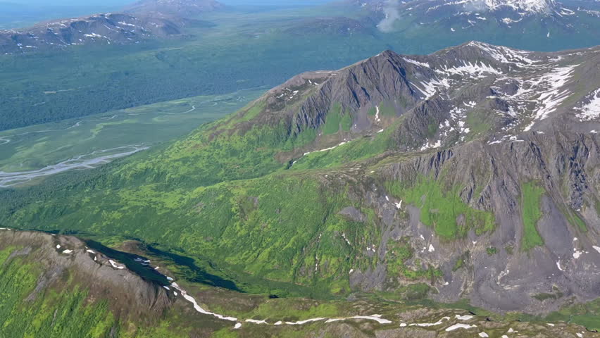 Flying over some of the green hills and snowcapped peaks in Denali National Park, Alaska