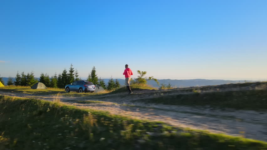 Young jogger trail running on wild mountain footpath while camping alone at beautiful sunrise