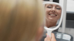 Closeup back view of blonde cheerful young woman patient smiling into mirror looking at healthy white teeth enjoying dental healthcare facilities in modern dentist office. Shooting in slow motion. - Powered by Shutterstock - Get 15% off with code: PIKWIZARD15