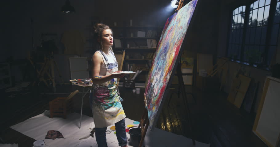 Millennial girl artist paints a picture in a loft studio puts paints on canvas with spatula. Abstraction cinematic. Creative thinking, non-standart view, a surge of bright emotions. Creative person Royalty-Free Stock Footage #1105910665