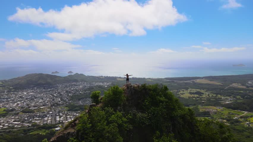 Drone view flying around young hiker standing on the top of ahiki hill at Olomana Three Peaks Hiking Trail in the mountain range in Oahu, Hawaii