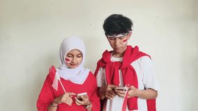 Attractive young student holds Indonesian flags and gesturing winning victory while having a good news on smartphone - Powered by Shutterstock - Get 15% off with code: PIKWIZARD15