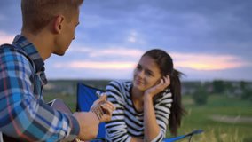 5 in 1 video! The couple (pair) sit near bonfire and camping tent: the man play on the guitar and woman drink tea and smile. Shot with crane and Red Cinema camera