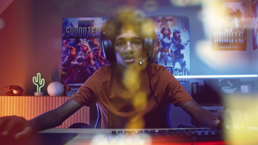 Portrait of teenage gamer in headphones playing shooter on computer at home. View from PC screen perspective with animated online video game. Gaming and cybersport. Futuristic VFX animation. Zoom out. Royalty-Free Stock Footage #1105916827