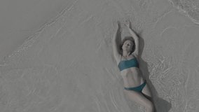 Top view of a girl lying on the beach and being washed by the waves of the sea. Absolutely clean and transparent water. Aerial view of tropical beach, top view of white sand tropical beach. Footage wi