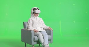 Horizontal shot on green screen background. VR or AR online at home. Cute girl in virtual reality googles in chair. Woman clicks invisible buttons and pulls virtual sliders. Beautiful woman have fun.