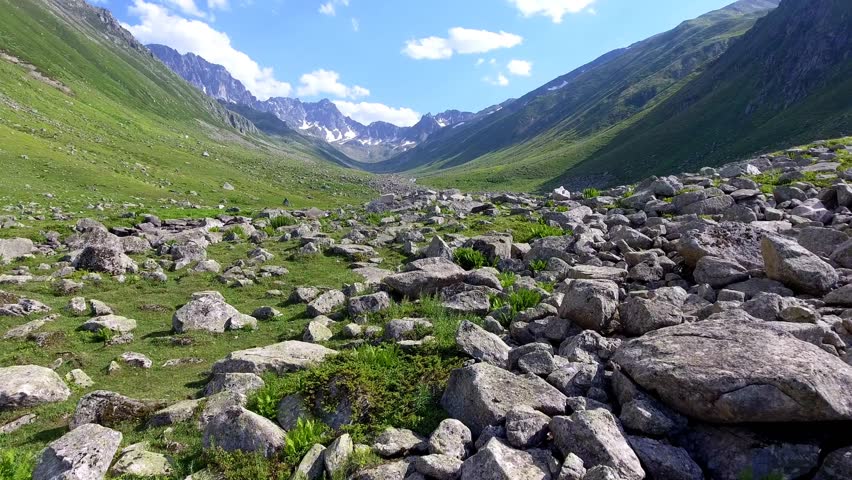 Aerial view of u-shaped valley stream and green meadows in treeless high altitude alpine region.