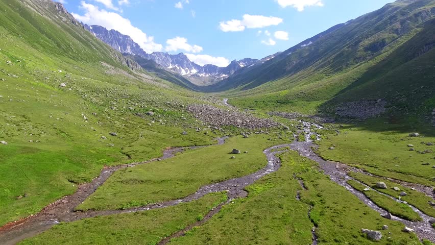 Aerial view of u-shaped valley stream and green meadows in treeless high altitude alpine region.