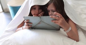Two child girls under blanket with digital tablet