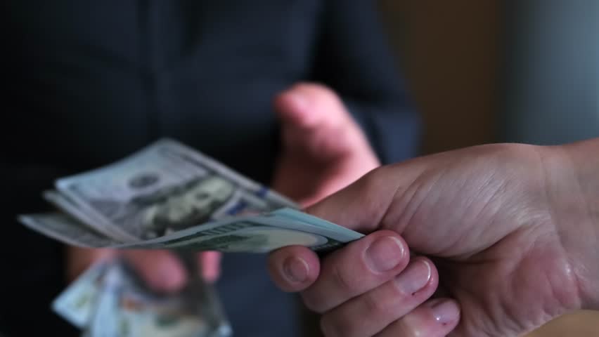 Businessman in a dark shirt taking profit from the transaction in cash US dollars. Concept of financial wealth, money, and power.