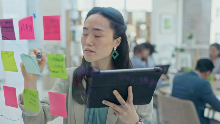 Asian woman, tablet and writing on glass board for schedule planning or sticky note tasks at office. Female person with technology in brainstorming, strategy or mind map for project plan at workplace Royalty-Free Stock Footage #1105934091