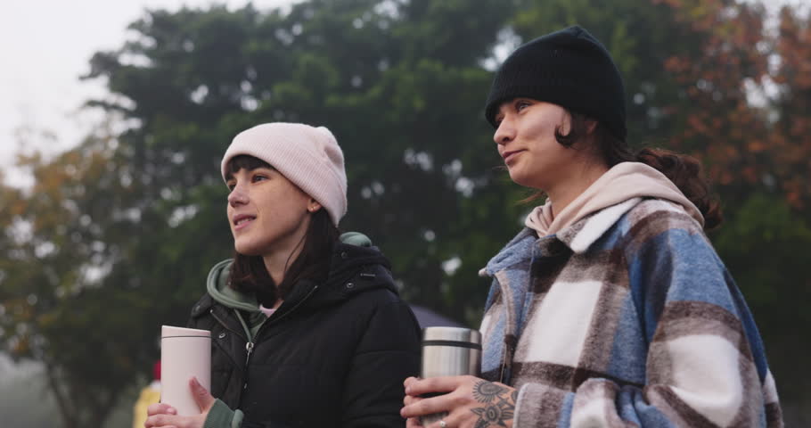 Girl, together and talking at camp with coffee in morning for travel or relax on weekend. Nature, women and hot beverage in environment for adventure or hike on vacation with conversation in woods.