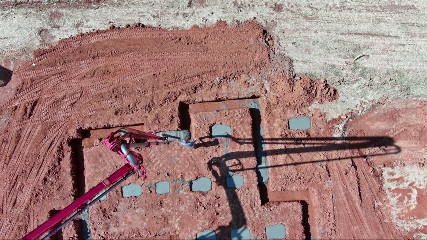 Wet concrete is being directed into house foundation by builder using concrete pump.