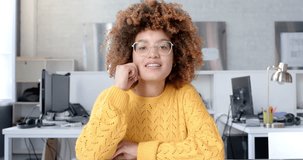 Happy biracial casual businesswoman with afro in glasses having video call at office, slow motion. Business, work, communication and casual office, unaltered.