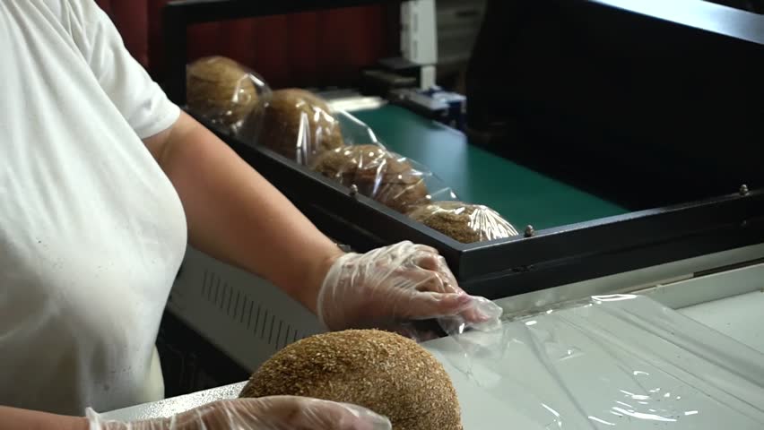 A female bakery worker packs sliced ​​bread using a specialized packaging machine. Packaging of bakery products before sending to the store shelves. Royalty-Free Stock Footage #1105938797