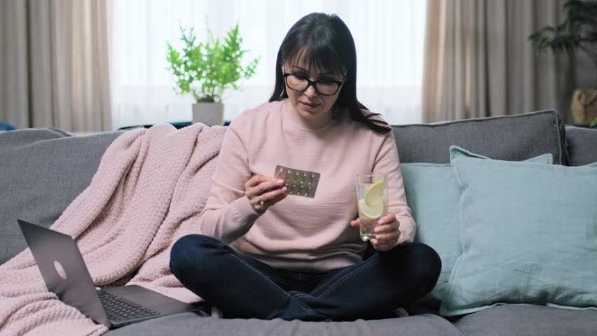 Mature woman taking omega-3 capsule while sitting on sofa at home