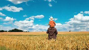 Young father and son in wheat field with blue sky and clouds on background