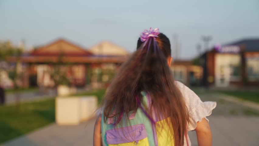 little girl with long hair runs city park. children leg jogging. child school backpack run along city road park. happy family. little girl daughter runs along sidewalk city. school road backpack.