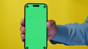 Hands Holding Mobile Phone with Green Screen on Yellow Background. Mobile Phone with Green Screen and Color Key. Ideal for Product Placement.