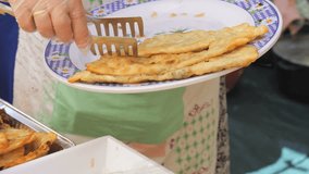 A woman lays out flat cakes with meat-filled dough on a large tray. Chebureki