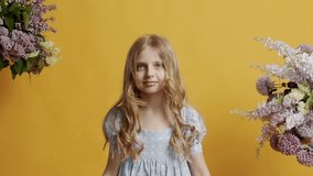 The 7 year old little girl is dressed in a light blue dress and looks beautifully into the room on a yellow background in the studio. Beautiful little girl looking at the camera and smiling kindly.