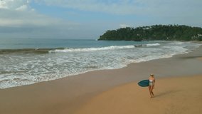 Woman surfer in bikini holds surfboard walks on beach by ocean aerial view. Young caucasian female in swimsuit carries surfing board along tide at sea shore in tropical location view from drone - Powered by Shutterstock - Get 15% off with code: PIKWIZARD15