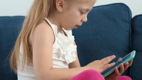The child plays in an electronic wireless tablet, side view. Watch a child who plays and is addicted to gadgets. Undistractedly look at the screen. Modern smart developing child