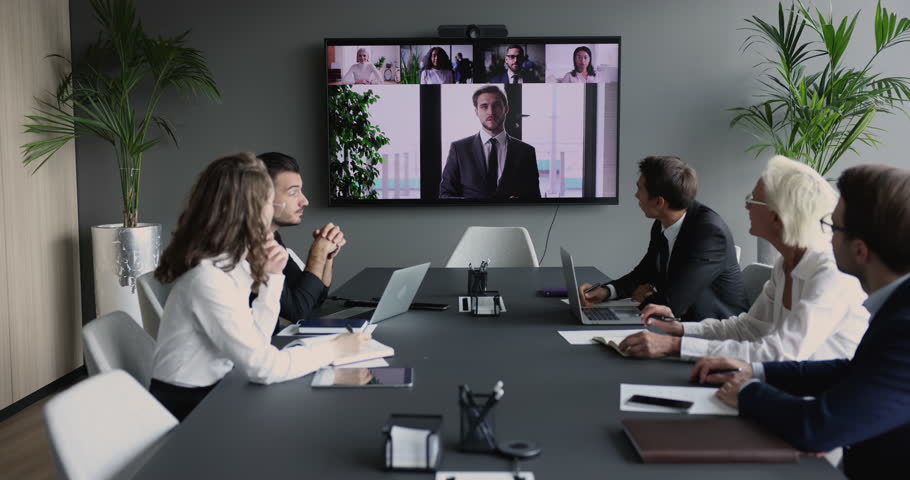Business group meeting at conference table, looking at large display with head shots of speaking colleagues, using Internet technology for remote teamwork. Boss talking to team on video call Royalty-Free Stock Footage #1105962963