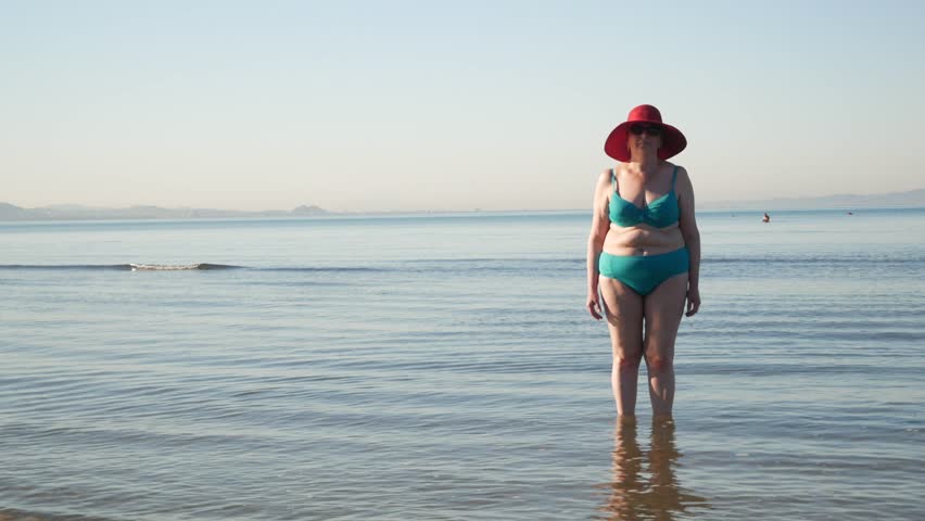 body positive senior woman in sunglasses wearing in swimsuit and summer hat on the sea beach,  Outdoors