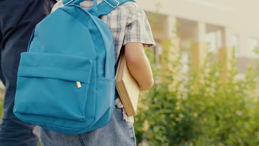 Little boy with briefcase, book holds dads hand on way school. Briefcase on kid back. New school backpack for first grader. Happy student with book, school bag goes to class. Beautiful school backpack Royalty-Free Stock Footage #1105972767