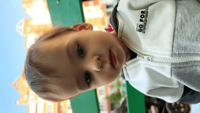 Beautiful Caucasian baby sitting on the bench outdoors. Kid takes a cap from dad's head and puts it on. Close up. Vertical video.