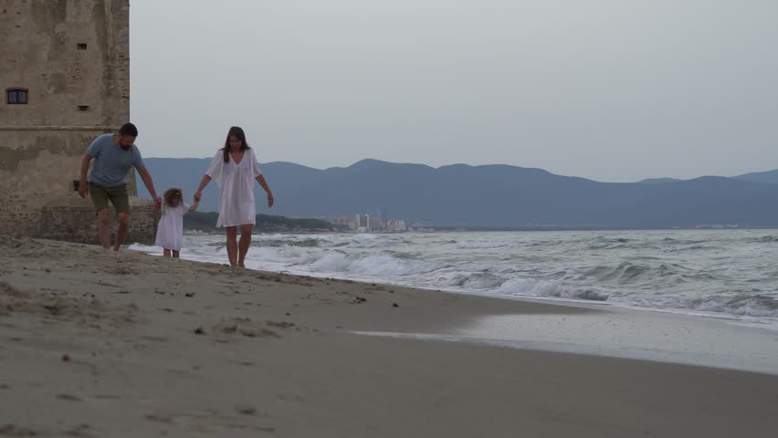 Italy, Tuscany. Mother, father and 3 year old daughter running on the beach holding hands in the evening