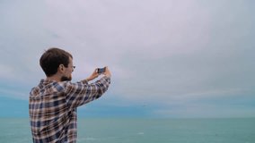 Man holds smartphone, takes photo or shoots video of arriving passenger airplane, airliner against the overcast sky - back view, wide angle view. Photography, plane spotting and technology concept