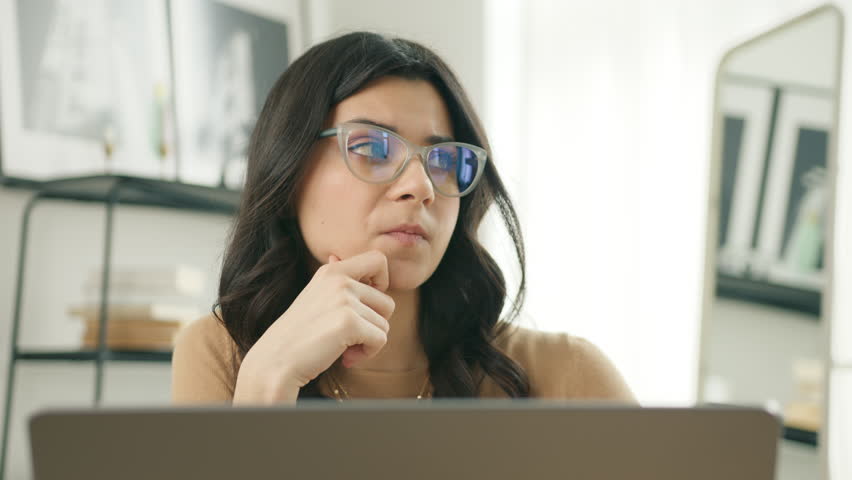 Thoughtful serious young latino woman writer in glasses sitting at home office desk with laptop. Girl thinking of inspiration, searching problem solution ideas, lost in thoughts, dreaming looking away Royalty-Free Stock Footage #1105985191