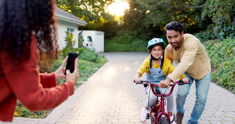 Mother, father and kid on bike learning in driveway with phone to record video, photograph or family support. Excited parents teaching happy girl on bicycle with mobile for memory, fun games and care