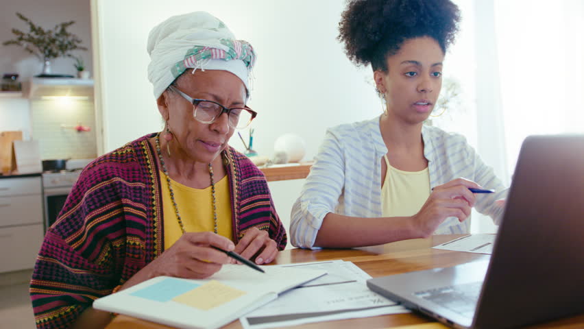 Young African-American woman using laptop, talking with senior mother sitting with papers, helping her with personal finances or pension income planning during the day at home Royalty-Free Stock Footage #1105987469