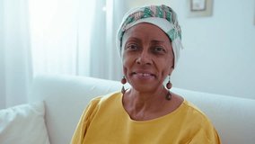 Senior black woman wearing headwrap and ethnic earrings looking at camera and smiling, posing on camera at home. Video portrait - Powered by Shutterstock - Get 15% off with code: PIKWIZARD15