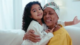 Happy senior black grandmother and cute little granddaughter hugging each other with love, posing on camera and smiling in the living room at home, girl holding silver piggy bank. Video portrait - Powered by Shutterstock - Get 15% off with code: PIKWIZARD15