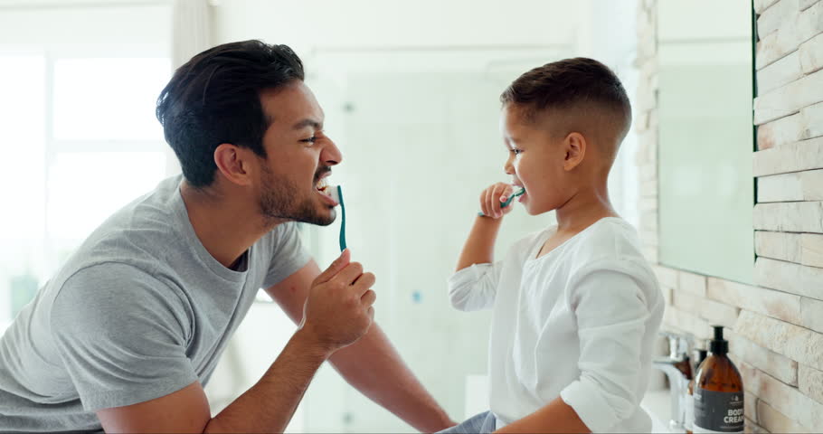 Dad, boy child and brushing teeth in bathroom for dental wellness, morning routine or teaching healthy habits. Family of father, kid and cleaning mouth with toothbrush for self care of fresh breath Royalty-Free Stock Footage #1105989977
