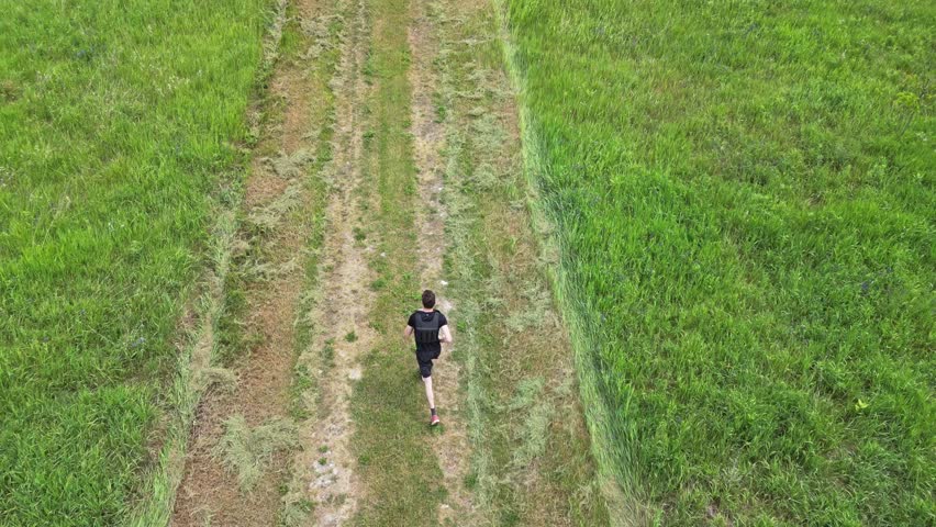 Jogger On Isolated Dirt Road Between Verdant Landscape. Aerial Tilt-up