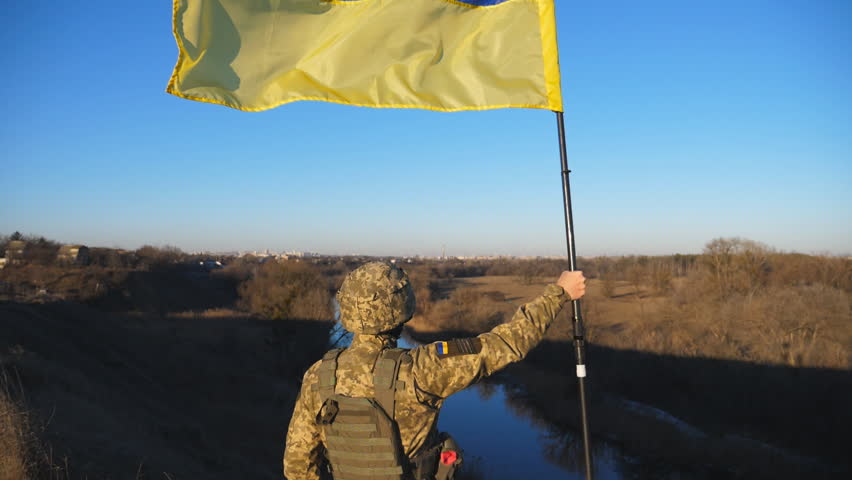 Male ukrainian army soldier lifted blue-yellow banner in honor of the victory against russian aggression. Young man in camouflage uniform raised a waving flag of Ukraine at countryside. End of war Royalty-Free Stock Footage #1106000621